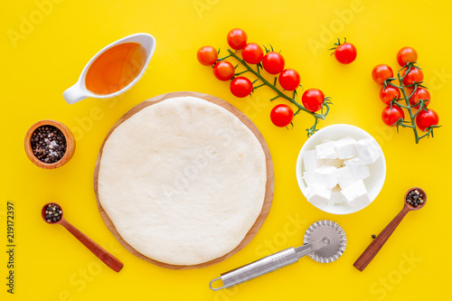 Ingredients for cooking pizza. Rolled out pizza dough  cherry tomatoes  olive oil  cheese mozzarella  spices on yellow background top view mockup
