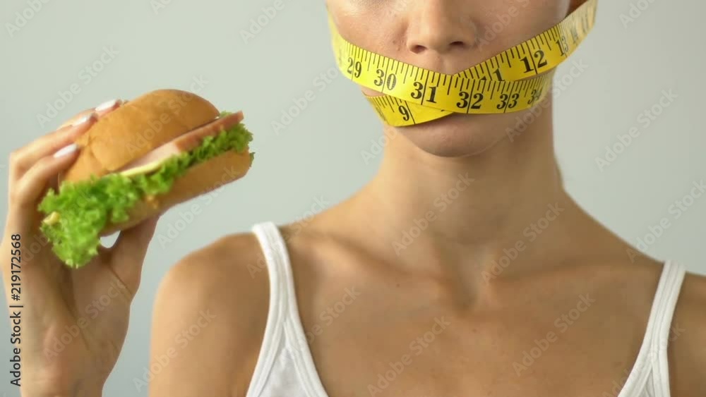 Female mouth wrapped with tape-line, girl wants burger but afraid of calories