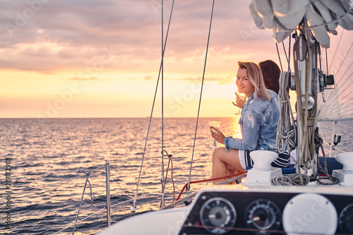 Female friends relaxing on the yacht with glasses of wine in the hands, during sunset on the high seas. © Fxquadro