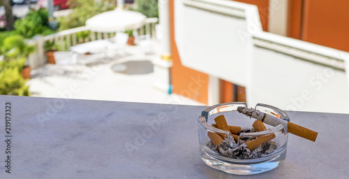 Smoldering cigarette lying on the ashtray. Ashtray and cigarette against the background of the garden. Ashtray and cigarette on the balcony.