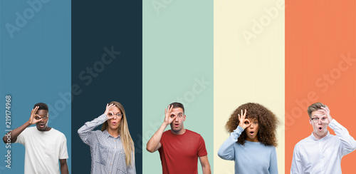 Group of people over vintage colors background doing ok gesture shocked with surprised face, eye looking through fingers. Unbelieving expression.