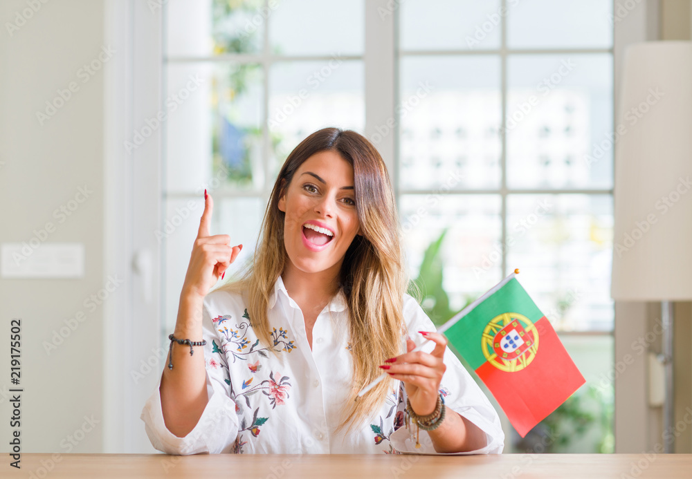 Young woman at home holding flag of Portugal surprised with an idea or question pointing finger with happy face, number one Young woman at home holding flag of Portugal surprised with an idea or question pointing finger with happy face, number one