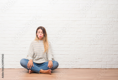 Young adult woman sitting on the floor over white brick wall at home depressed and worry for distress, crying angry and afraid. Sad expression.