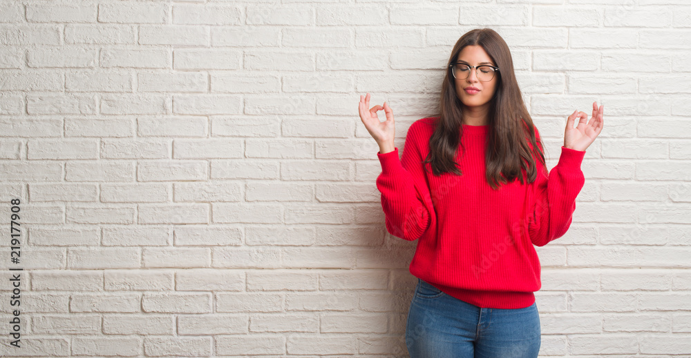 Young brunette woman standing over white brick wall relax and smiling with eyes closed doing meditation gesture with fingers. Yoga concept. Young brunette woman standing over white brick wall relax and smiling with eyes closed doing meditation gesture with fingers. Yoga concept.