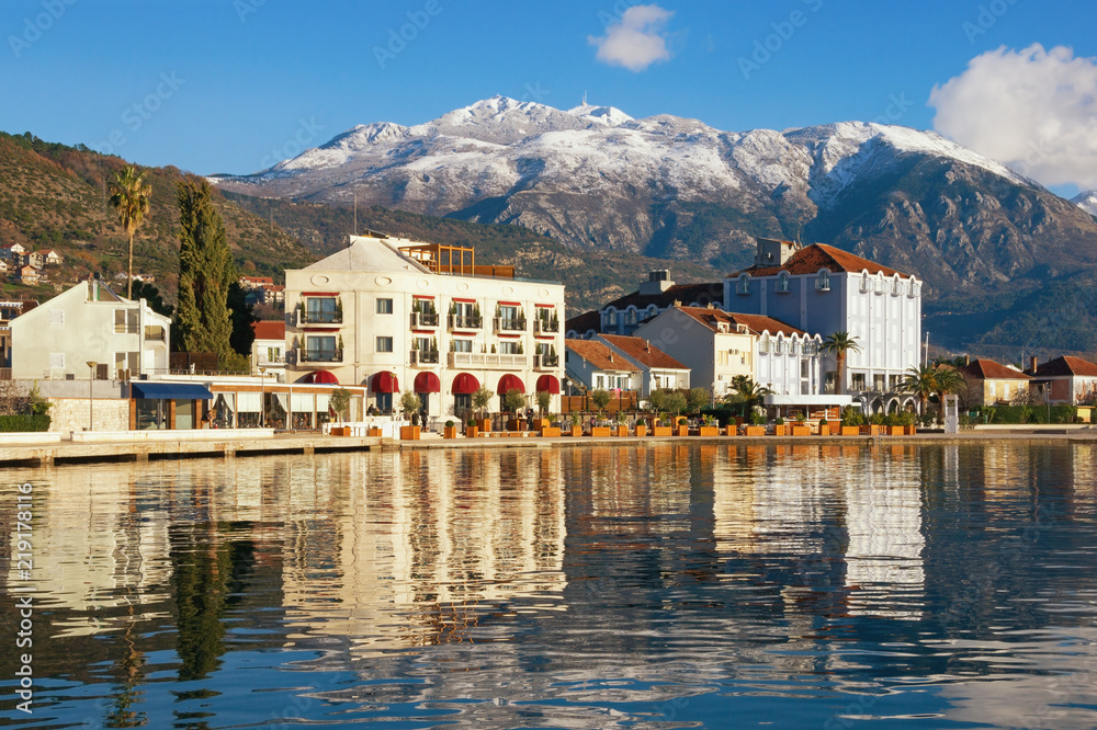 Sunny winter Mediterranean landscape. Montenegro, embankment of Tivat city and snow-capped peaks of Lovcen mountain