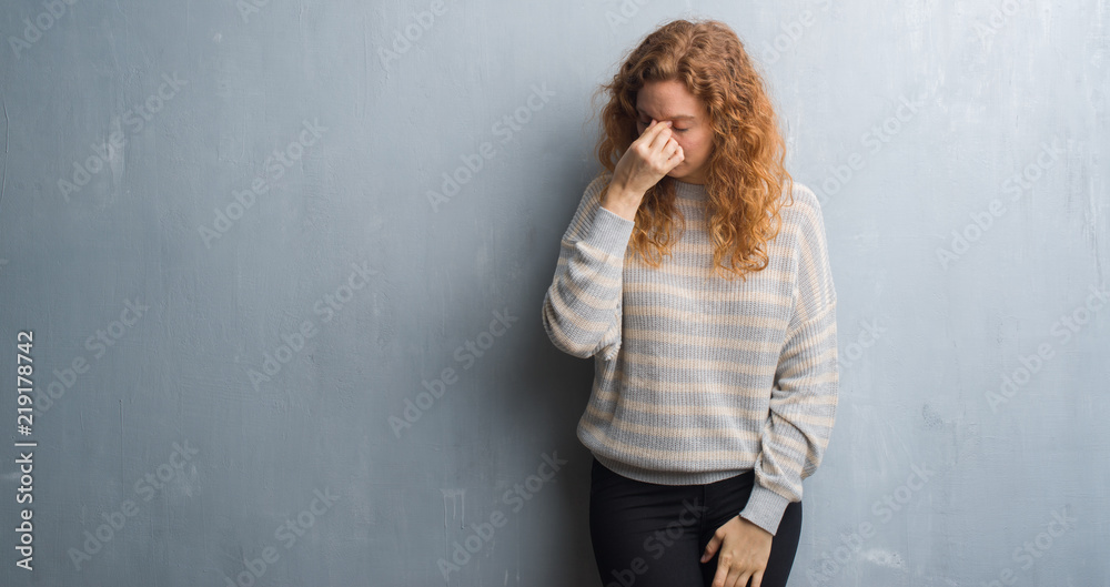 Young redhead woman over grey grunge wall tired rubbing nose and eyes feeling fatigue and headache. Stress and frustration concept.