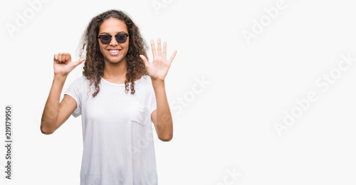 Young hispanic woman wearing sunglasses showing and pointing up with fingers number six while smiling confident and happy.