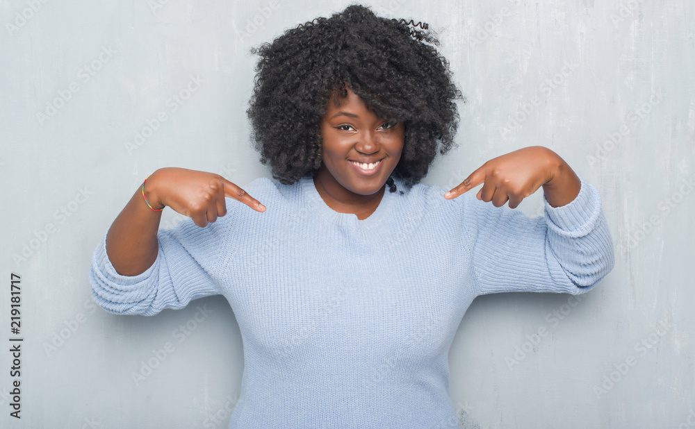 Young african american woman over grey grunge wall wearing winter sweater looking confident with smile on face, pointing oneself with fingers proud and happy. Young african american woman over grey grunge wall wearing winter sweater looking confident with smile on face, pointing oneself with fingers proud and happy.