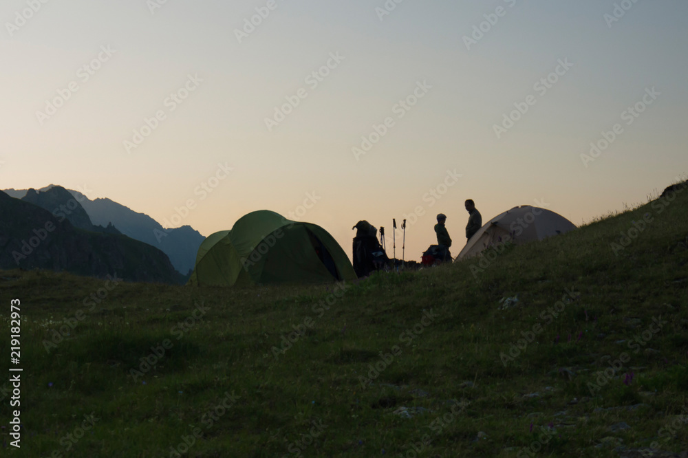 silhouettes of a boy and a man standing next to the tents on the background of the mountains