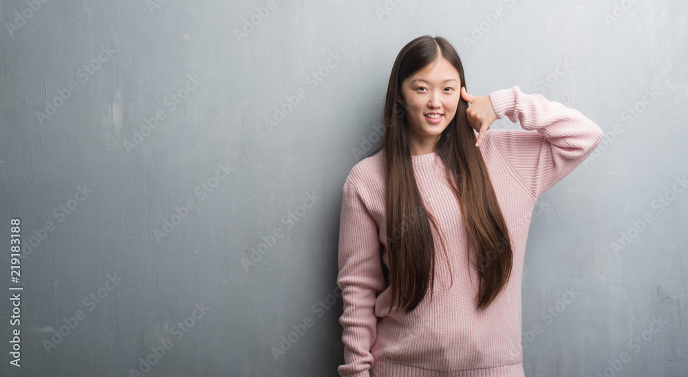 Young Chinese woman over grey wall smiling doing phone gesture with hand and fingers like talking on the telephone. Communicating concepts. Young Chinese woman over grey wall smiling doing phone gesture with hand and fingers like talking on the telephone. Communicating concepts.