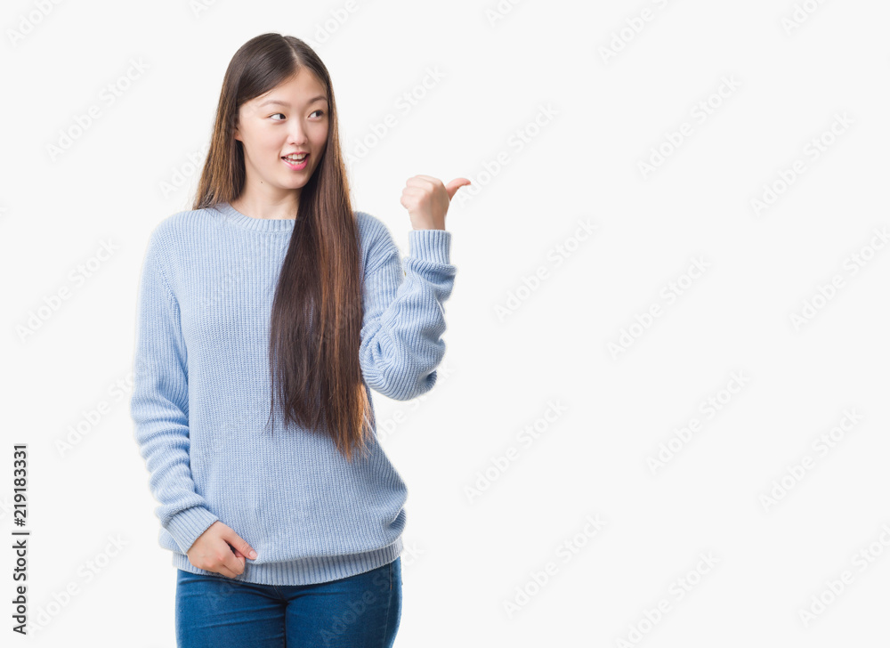 Young Chinese woman over isolated background smiling with happy face looking and pointing to the side with thumb up. Young Chinese woman over isolated background smiling with happy face looking and pointing to the side with thumb up.