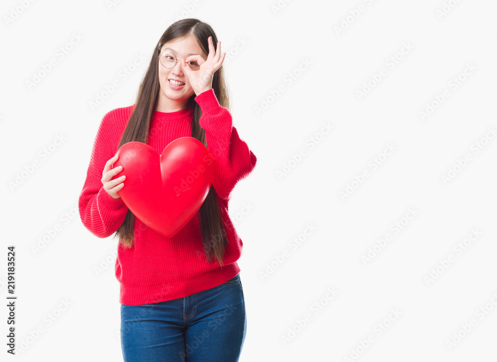 Young Chinese woman wearing graduate uniform red heart with happy face smiling doing ok sign with hand on eye looking through fingers Young Chinese woman wearing graduate uniform red heart with happy face smiling doing ok sign with hand on eye looking through fingers