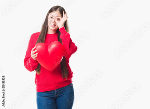 Young Chinese woman wearing graduate uniform red heart with happy face smiling doing ok sign with hand on eye looking through fingers © Krakenimages.com