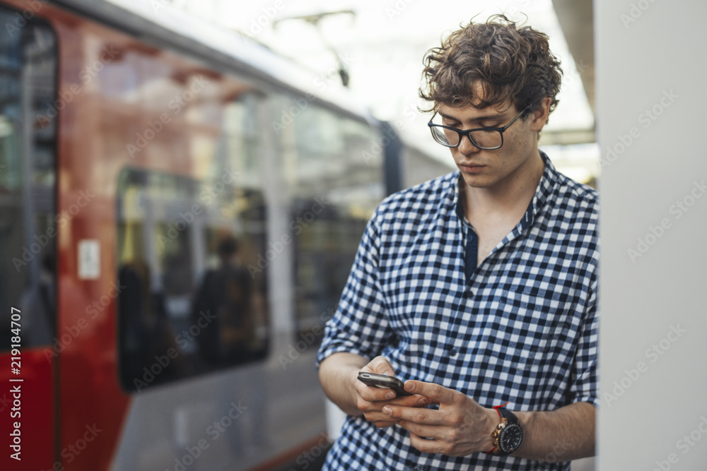 Distant plan of man looking at mobile phone while waiting train in metro station Distant plan of man looking at mobile phone while waiting train in metro station