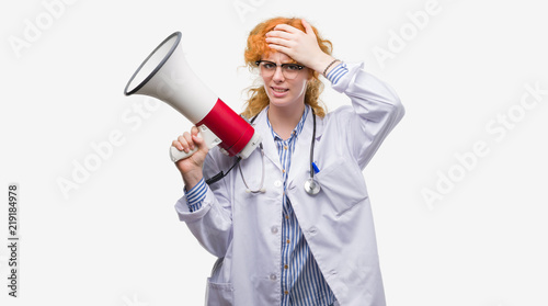 Young redhead doctor woman holding megaphone stressed with hand on head, shocked with shame and surprise face, angry and frustrated. Fear and upset for mistake.