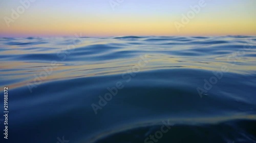 Slow motion rising up from underwater to smooth ocean waves at sunset. Emerging from surface of the sea to orange sky and calm soothing waters. Reaching above water level to gasp air to breathe. photo