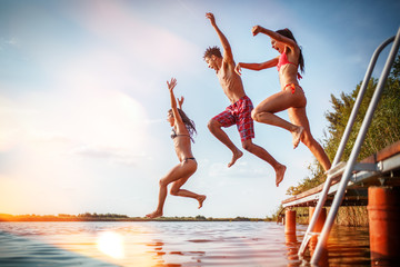Group of friends jumping into the lake from wooden pier.Having fun on summer day.