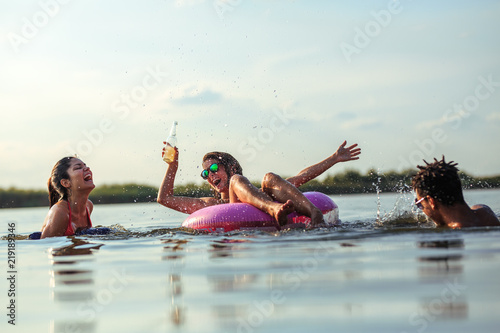 Young friends swimming and having fun in the lake.Female sitting on air mattress drinks lemonade and having fun with friends.