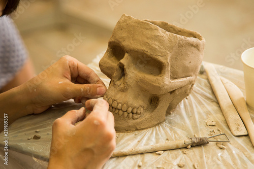 Sculptor modeling a skull out of raw clay with hands in a sculpting studio workshop