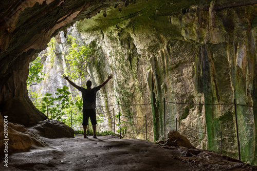 Картината върху платно Silueta de un hombre de pie con los brazos extendidos dentro de una cueva mirando hacia el exterior