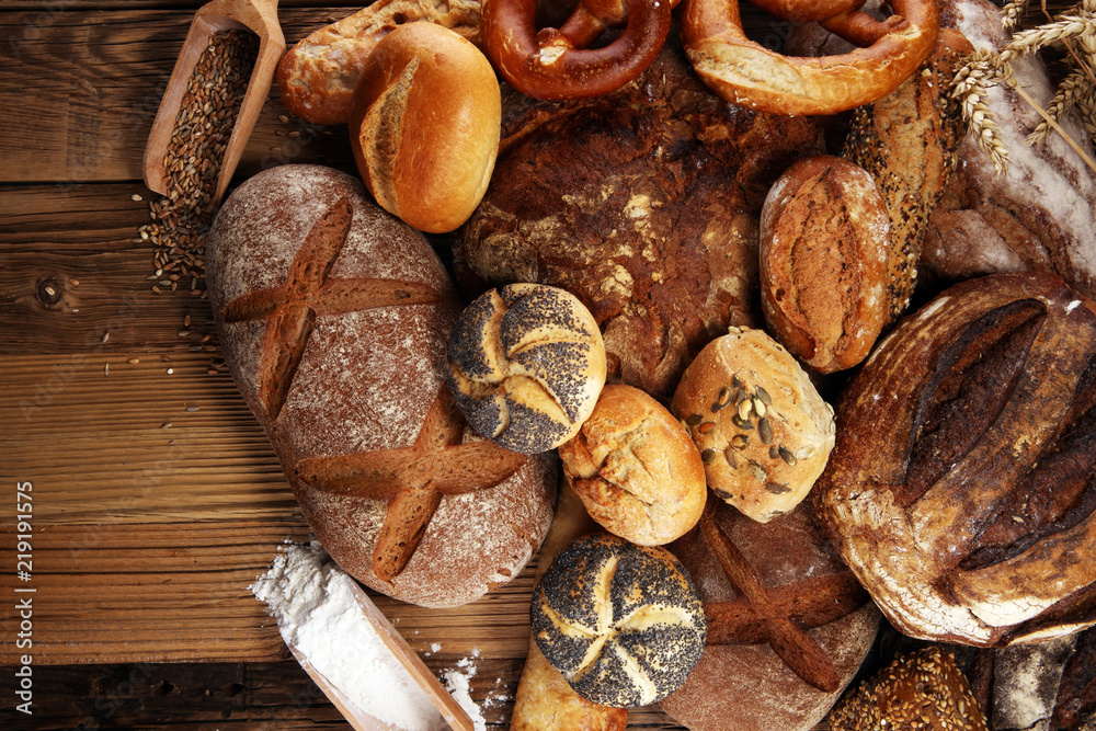 Different kinds of bread and bread rolls on board from above. Kitchen or bakery Different kinds of bread and bread rolls on board from above. Kitchen or bakery