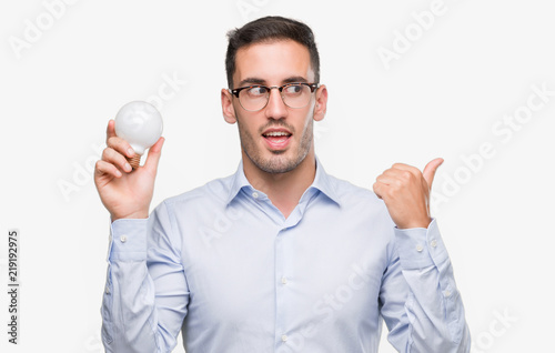 Handsome young man holding lightbulb as idea pointing with hand and finger up with happy face smiling