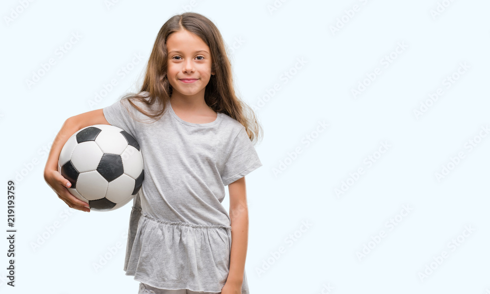 Brunette hispanic girl holding soccer football ball with a happy face standing and smiling with a confident smile showing teeth