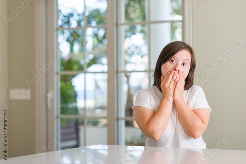 Down syndrome woman at home shocked covering mouth with hands for mistake. Secret concept.