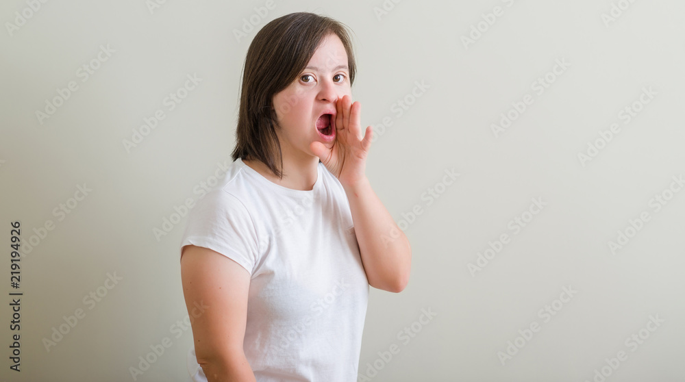 Down syndrome woman standing over wall shouting and screaming loud to side with hand on mouth. Communication concept. Down syndrome woman standing over wall shouting and screaming loud to side with hand on mouth. Communication concept.