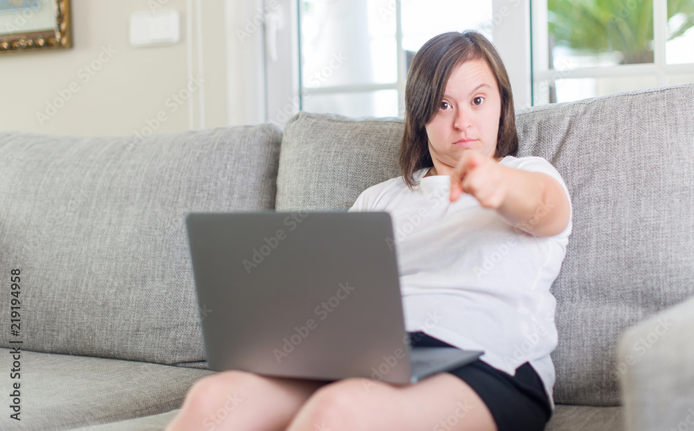 Down syndrome woman at home using computer laptop pointing with finger to the camera and to you, hand sign, positive and confident gesture from the front Down syndrome woman at home using computer laptop pointing with finger to the camera and to you, hand sign, positive and confident gesture from the front