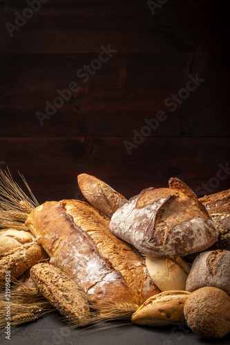 Composition of abundance of freshly baked loaves of bread and buns with ears of wheat