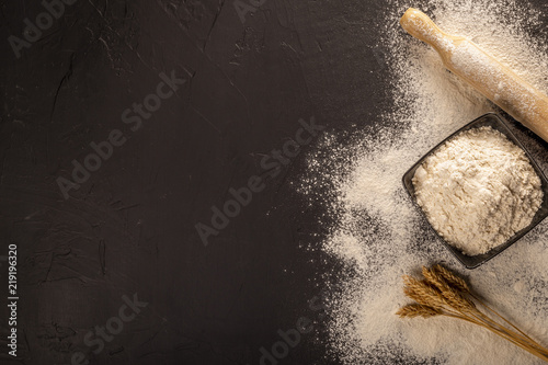 From above shot of arranged bowl of flour on black table with rolling pink and wheat
