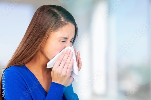 Brunette woman sneezing in a tissue on blurred background