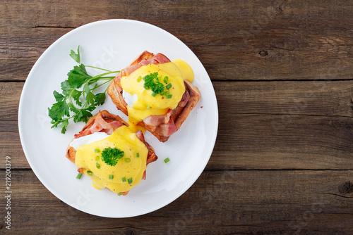 Eggs benedict with bacon on wooden background . Top view  photo