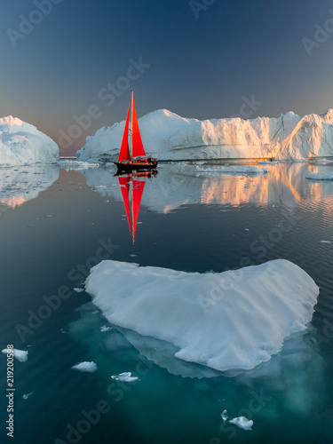 Greenland midnight Sunset iceberg mirror with red sail ship	 photo