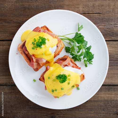 Eggs benedict with bacon on wooden background . Top view  photo