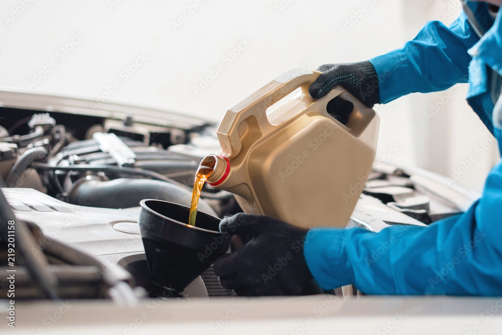The auto mechanic pours new clean engine oil through the funnel. replacement of engine oil in the machine. car service worker