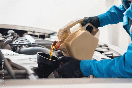 Obraz na płótnie The auto mechanic pours new clean engine oil through the funnel. replacement of engine oil in the machine. car service worker w salonie