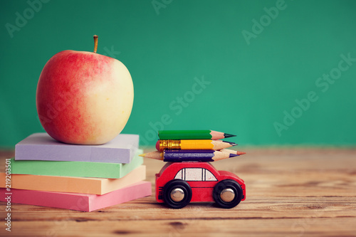 Miniature Red Car Carrying a colorful pencils and red apple and stack papers on wooden table. Back to school concept
