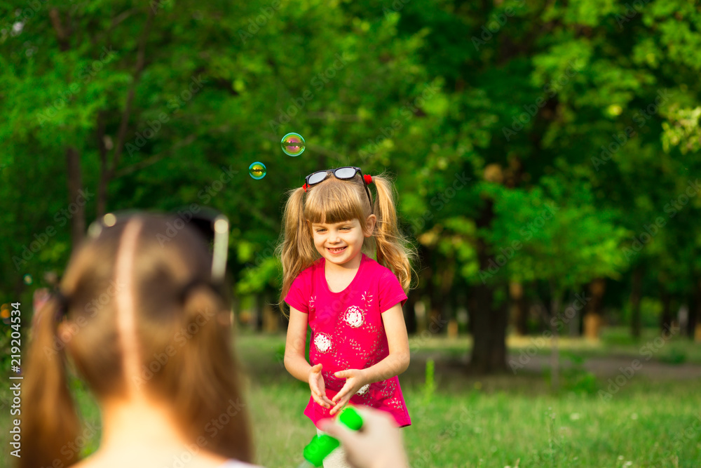 Young mother and little daughter playing in park with soap bubbles. Love family, parenthood, childhood Young mother and little daughter playing in park with soap bubbles. Love family, parenthood, childhood