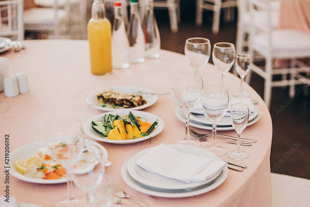 stylish wedding setting, tender pink table with wine glasses, cutlery, napkin and delicious food and drinks. luxury catering in restaurant. modern wedding reception