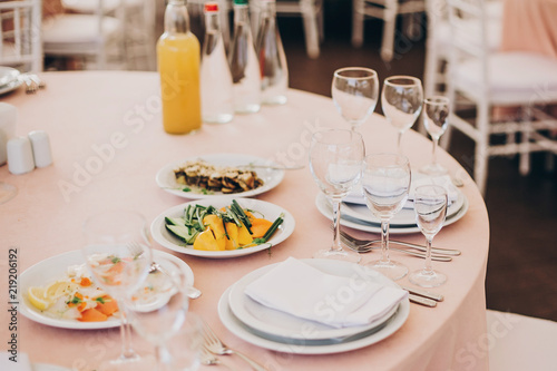 stylish wedding setting, tender pink table with wine glasses, cutlery, napkin and delicious food and drinks. luxury catering in restaurant. modern wedding reception