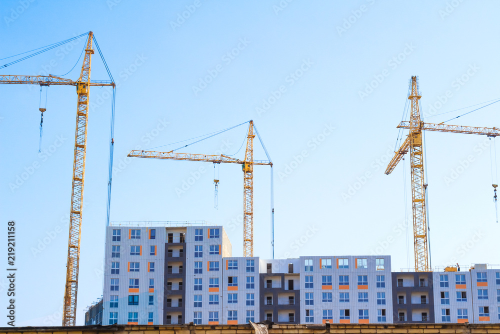 Building cranes and building under construction on blue sky