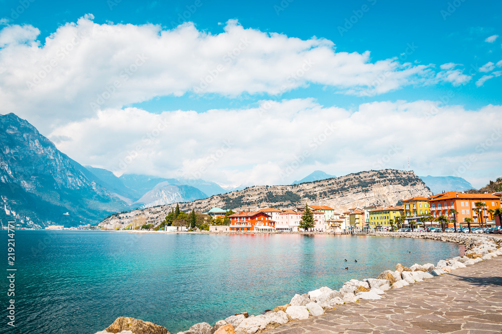 Harborside of town Torbole Lake Garda, promenade next to the lake with colorful houses and trees, Italy