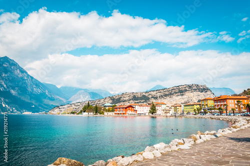 Harborside of town Torbole Lake Garda, promenade next to the lake with colorful houses and trees, Italy