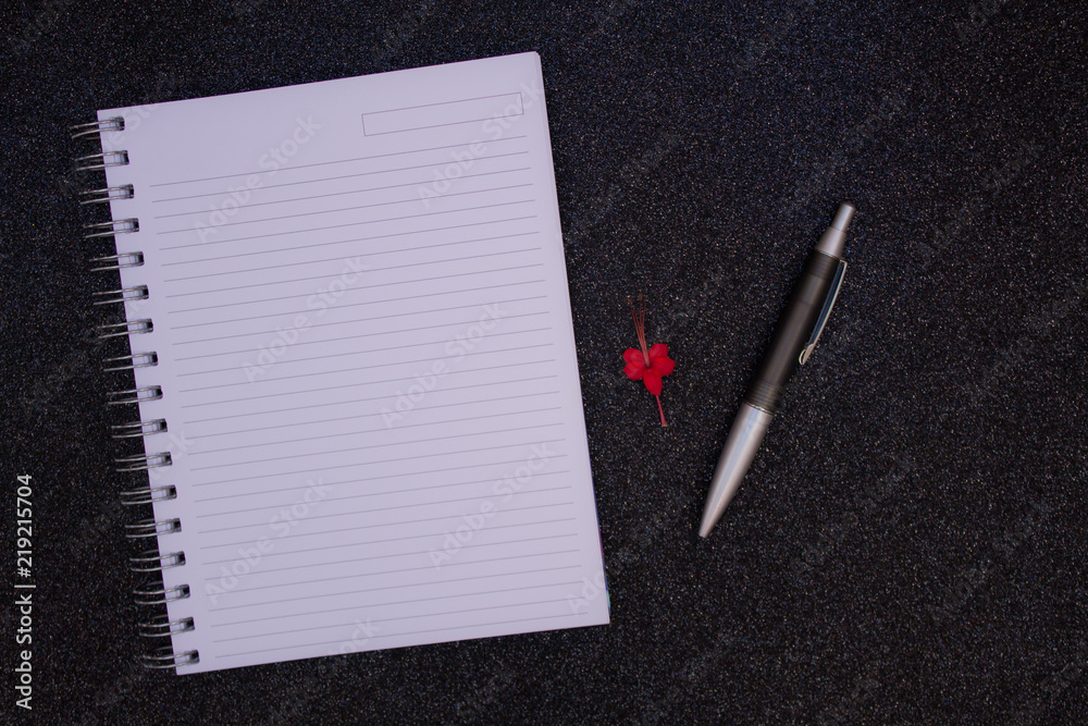NOTEBOOK WITH BLANK PAGE WITH RED FLOWER AND BLACK PEN ON BLACK GLITTER BACKGROUND NOTEBOOK WITH BLANK PAGE WITH RED FLOWER AND BLACK PEN ON BLACK GLITTER BACKGROUND
