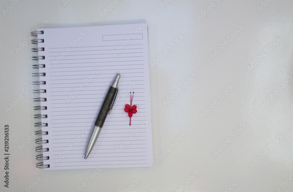 NOTEBOOK WITH BLANK PAGE WITH RED FLOWER AND BLACK PEN ON WHITE BACKGROUND NOTEBOOK WITH BLANK PAGE WITH RED FLOWER AND BLACK PEN ON WHITE BACKGROUND