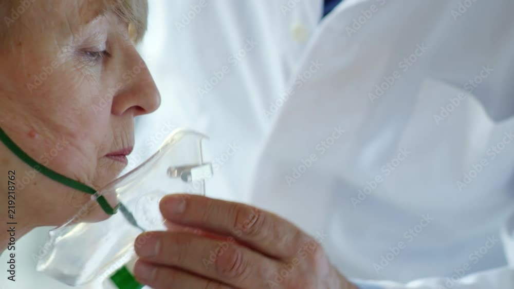 Close-up of hand of male doctor putting oxygen mask on face of middle-aged female patient Close-up of hand of male doctor putting oxygen mask on face of middle-aged female patient