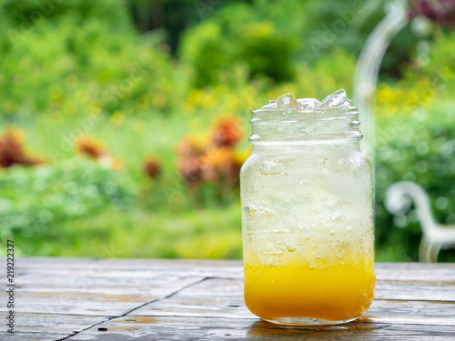 A fresh orange soda drink filled with ice in a vintage style glass container Full of ice in the glass. Placed on wooden desk in garden with a green background