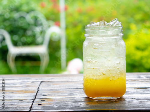 A fresh orange soda drink filled with ice in a vintage style glass container Full of ice in the glass. Placed on wooden desk in garden with a green background